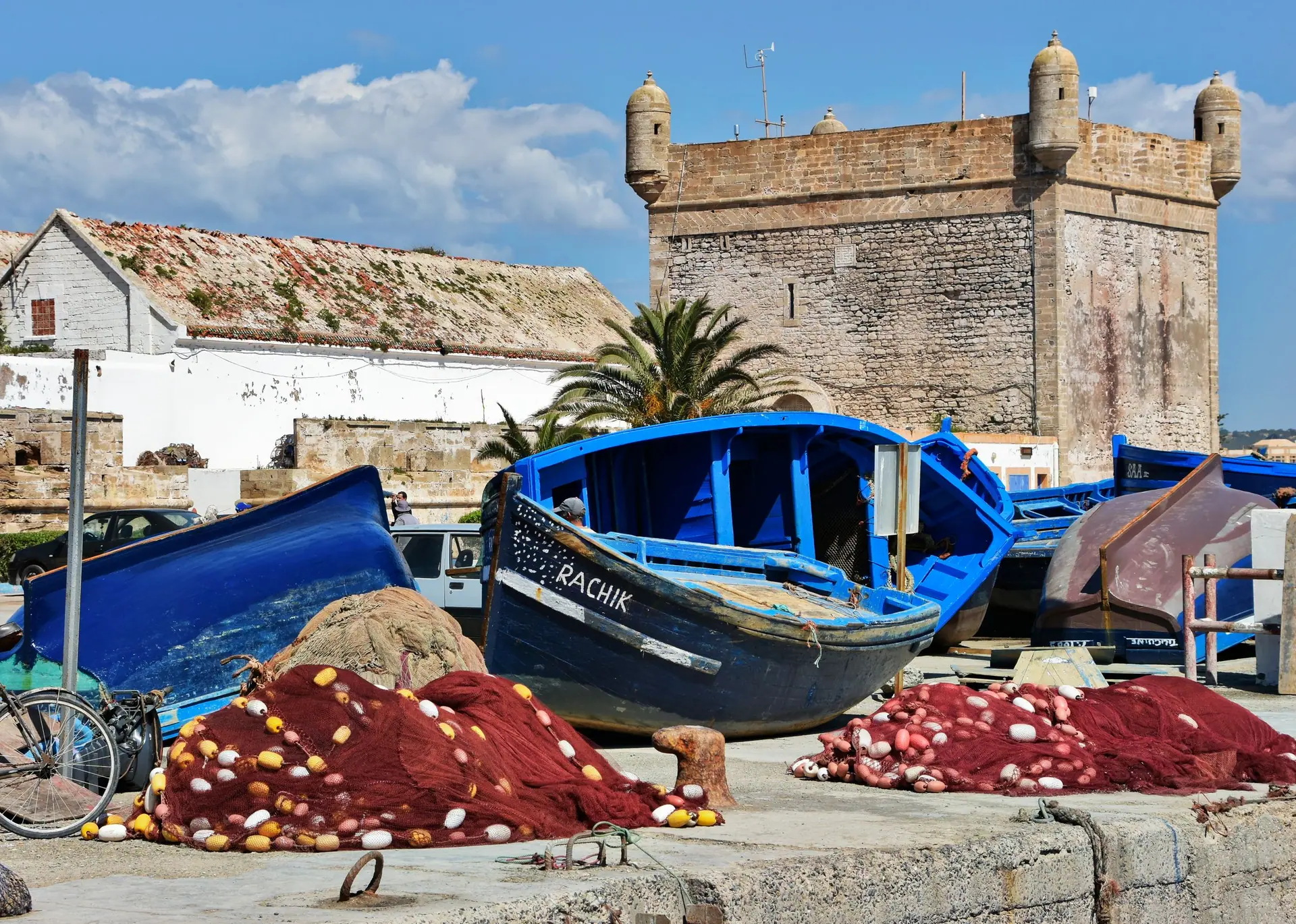 Colorful fishing boats and nets by the historic fort in Essaouira, Morocco, under a clear blue sky.