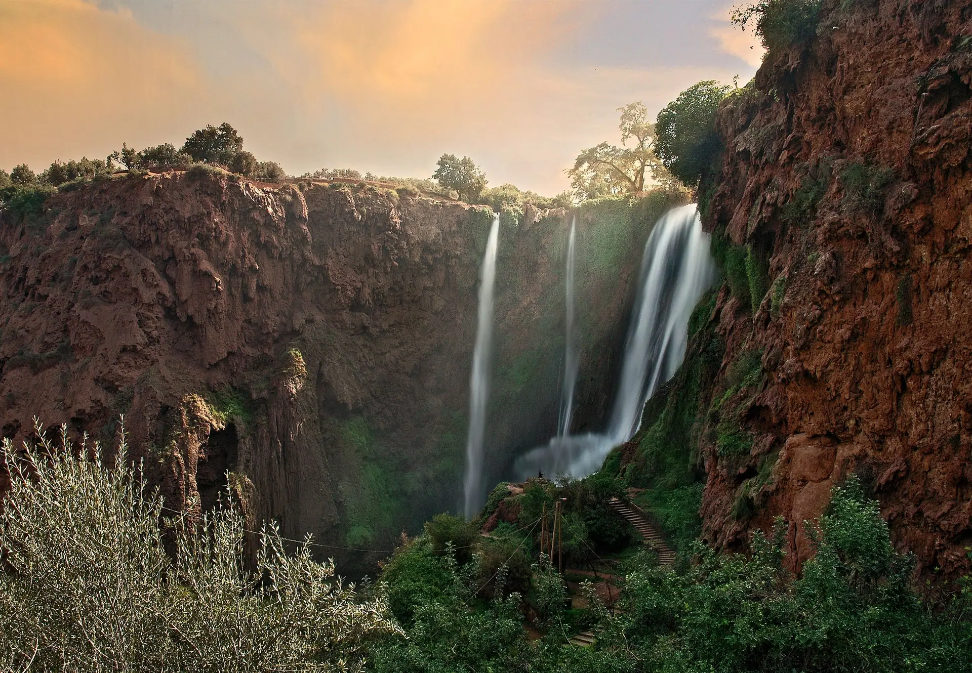 Beautiful view of Ouzoud Waterfalls cascading from red cliffs under a sunset sky in Morocco.